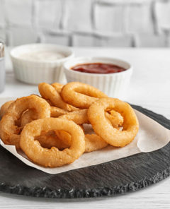 Slate plate with tasty onion rings on table