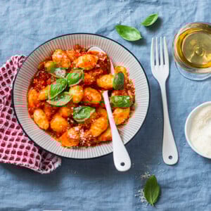 Potato gnocchi in tomato sauce with basil and parmesan and a glass of white wine on blue background, top view. Italian cuisine. Vegetarian food