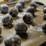 Small brown chocolate balls lay on a baking sheet sprinkled with powdered sugar and flour, the process of making gingerbread