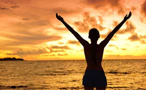 Silhouette of a woman with her arms up, embracing the sunset