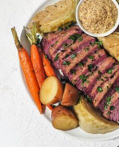 Classic Corned Beef on a platter with roasted carrots and cabbage.