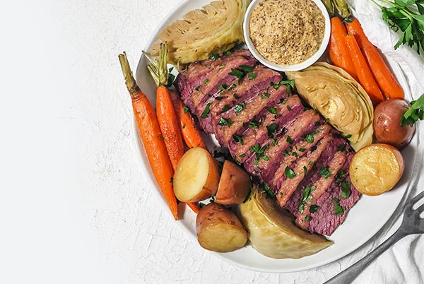 Classic Corned Beef on a platter with roasted carrots and cabbage.