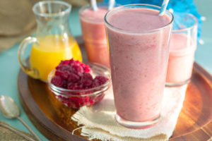 Pink colored detox smoothie on a wooden tray with smoothies in the background