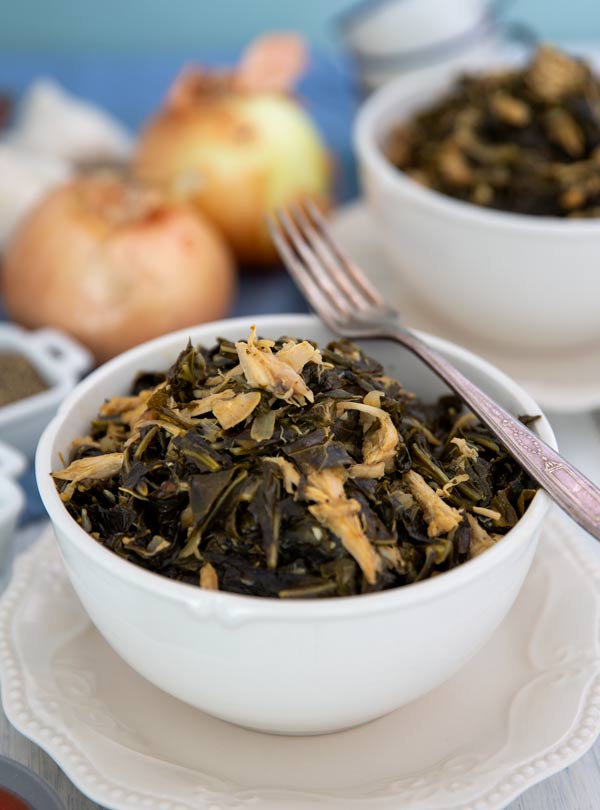 Healthy Southern Collard Greens in a white bowl with onions in the background