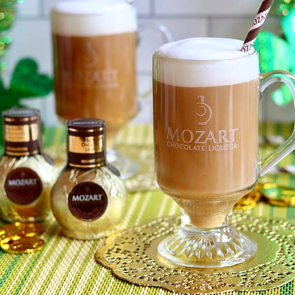 Mozart Chocolate Liqueur on a gold placemat with green clovers in the background for St. Patrick's Day