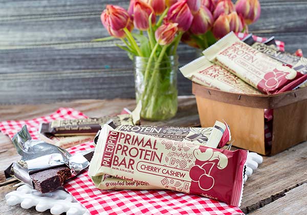Paleo Pro Primal Bars on a table and in a basket with flowers in the background