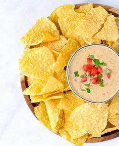 Queso Dip with corn tortilla chips around the bowl.