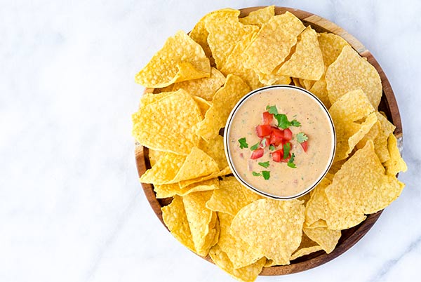 Queso Dip with corn tortilla chips around the bowl.