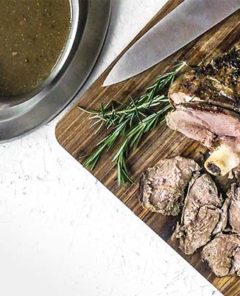 Slow Cooker Lamb on a cutting board with gravy on the side.