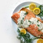 Slow Roasted Salmon on a plate with dill sauce and lemon slices.