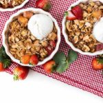 Strawberry Pineapple Crisp with strawberries scattered around on a red plaid tablecloth.