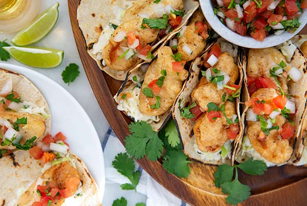 Baja Fish Tacos on a wooden serving platter with pico de gallo in a bowl