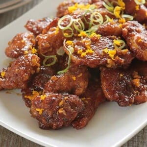 Orange Chicken on a white platter with orange zest on top