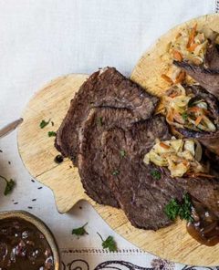 Rolled Sauerbraten on a wooden cutting board with cabbage on the side