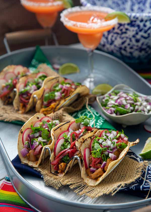 Vegan Barbacoa Tacos lined up on a plate with a margarita in the background