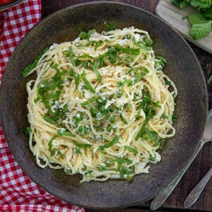 Gluten-Free Lemon and Pea Spaghetti on a dark colored plate with sliced lemons in the background and a red and white checkered napkin under the plate