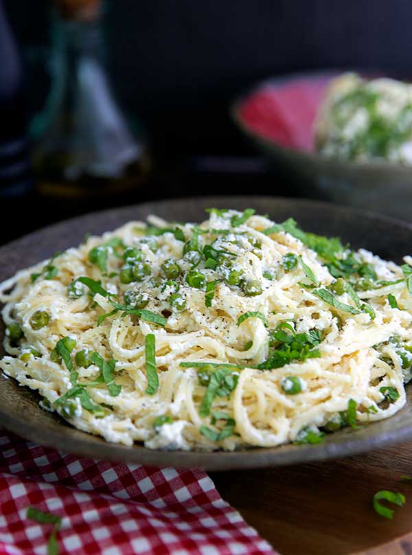 Closeup of Gluten-Free Lemon and Pea Spaghetti on a dark colored plate with a white and red checkered napkin in front