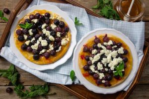 Apricot and Berry Flatbreads garnished with mint leaves on white plates on top of a wooden serving tray