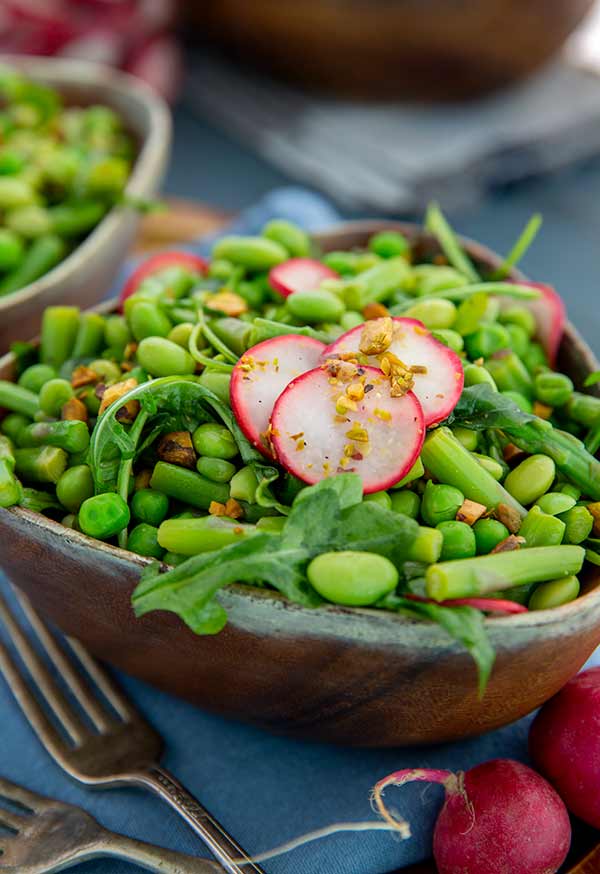 Close up of Asian Spring Pea and Asparagus Salad garnished with radishes in a wooden bowl with light blue napkins