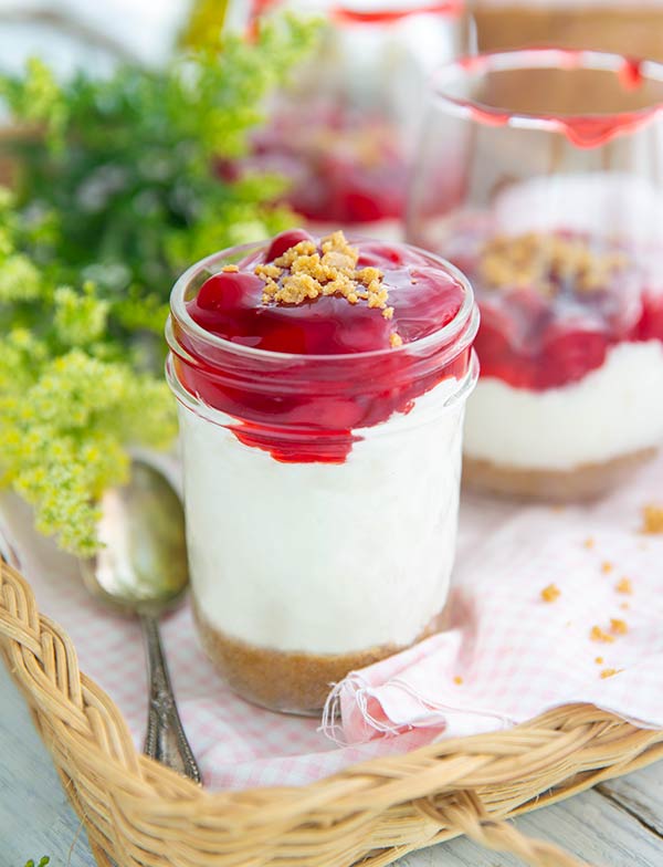 Cherry Cheesecake-in-a-Jar with bright green and yellow flowers in the background