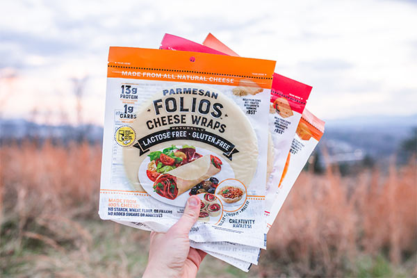 A hand holds up Folios Cheese Wraps in front of a field