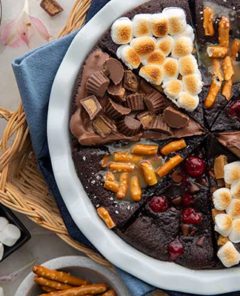 A gluten-free chocolate cake with each slice decorated with different toppings, including marshmallows on one, peanut butter cups on another, and more