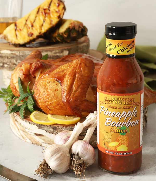 Silverton Pineapple Bourbon Sauce bottle in front of a roasted chicken with grilled pineapple in the background