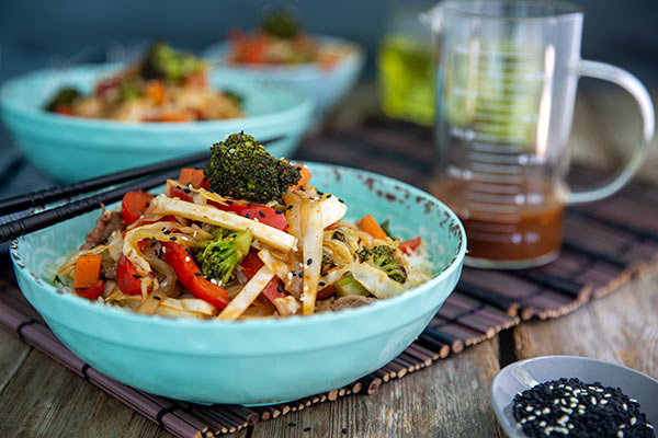 Spicy Beef and Vegetable Stir-Fry in a blue bowl with chop sticks on a bamboo placemat