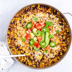 Beef Burrito Skillet Casserole in a stainless steel skillet topped with fresh jalapeno, tomatoes, and avocado
