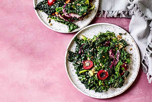 Bourbon Cherry Kale Salad on a white plate on a pink background