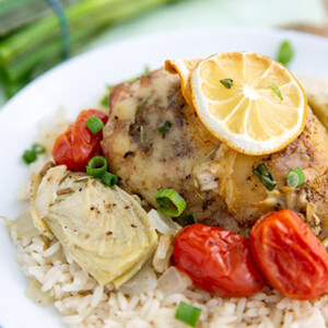Chicken & Artichokes with White Wine on a white plate served over rice with tomatoes and a lemon slice
