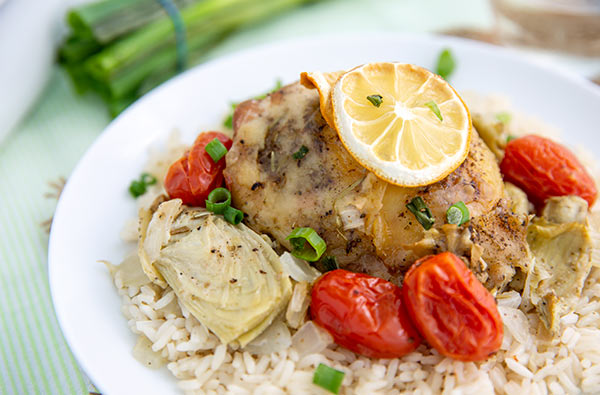 Chicken & Artichokes with White Wine on a white plate served over rice with tomatoes and a lemon slice