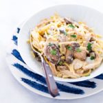 Chicken Tetrazzini in a white bowl on top of a white plate with dark blue streaks on it