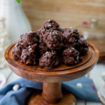 Chocolate Sunbutter Cookie Clusters on a wooden pedestal with a blue cloth napkin at the bottom and marshmallows in the background