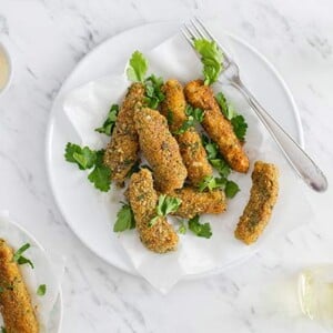 Paleo Crunchy Fish Sticks garnished with parsley on a white plate on a white and gray marble background