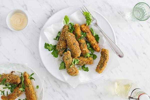 Paleo Crunchy Fish Sticks garnished with parsley on a white plate on a white and gray marble background