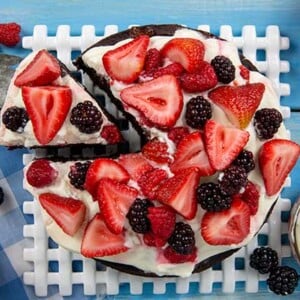 Grandma's Depression-Era Chocolate Cake with Berries on a white trivet on top of a blue background
