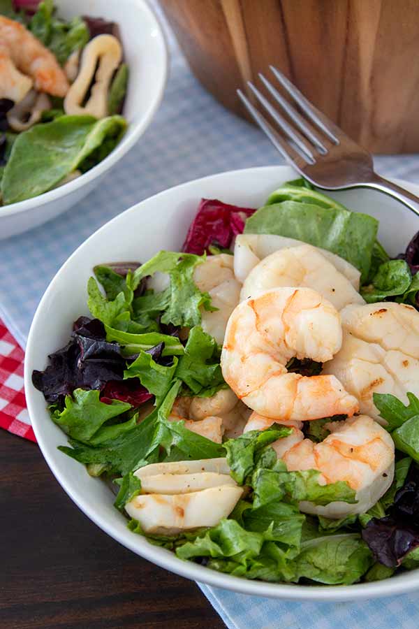 Grilled Seafood Salad in a white bowl with a light blue and white checkered towel underneath
