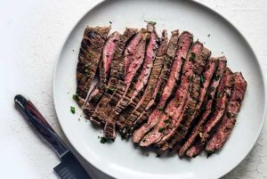 Herb-Marinated Flank Steak sliced into strips on a white plate
