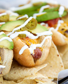 Nacho-inspired hot dogs on a bed of tortilla chips with a drizzle of sour cream and topped with sliced avocado