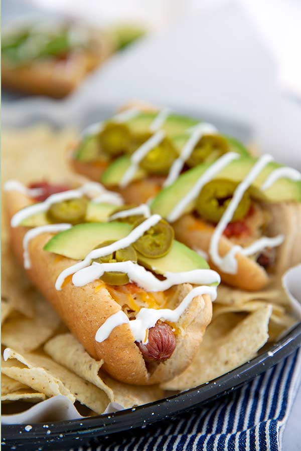Nacho-inspired hot dogs with cream sauces drizzled on top and jalapeno and avocado slices