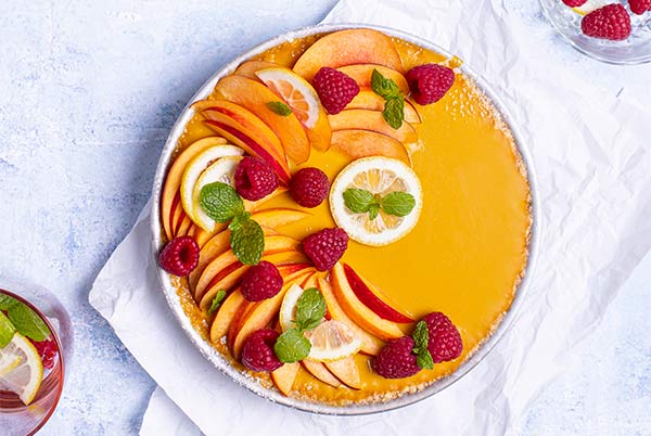 Peach & Mango No-Bake Pie decorated with fresh peach slices, lemon slices, raspberries, and mint