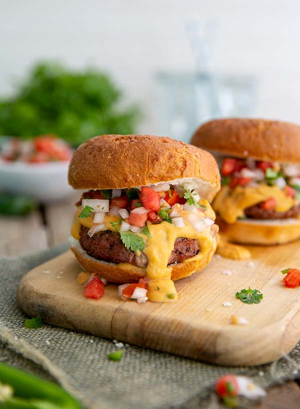 Plant-Based Queso Burger with queso dripping out onto a wooden cutting board