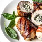 Prosciutto-Wrapped Stuffed Chicken on a white plate with basil leaves as garnish