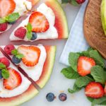 Round slice of watermelon cut into triangles to form a pizza, topped with yogurt and berries