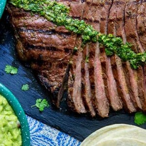 Carne Asada sliced into strips with chimichurri on top on a slate serving tray