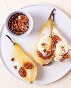 Cider Poached Pears topped with ice cream and walnuts on a white plate on a beige background