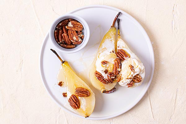 Cider Poached Pears topped with ice cream and walnuts on a white plate on a beige background