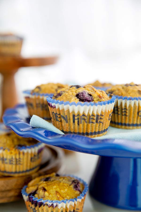 Double Berry Pecan Muffins in muffin papers that say gluten free on them on top of a royal blue cake pedestal