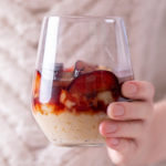 Woman's hand holding out a wine glass with rice pudding and plums in it